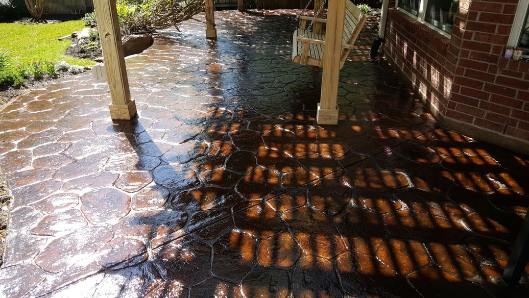 Stamped concrete patio with a glossy finish, surrounded by greenery and shaded seating.