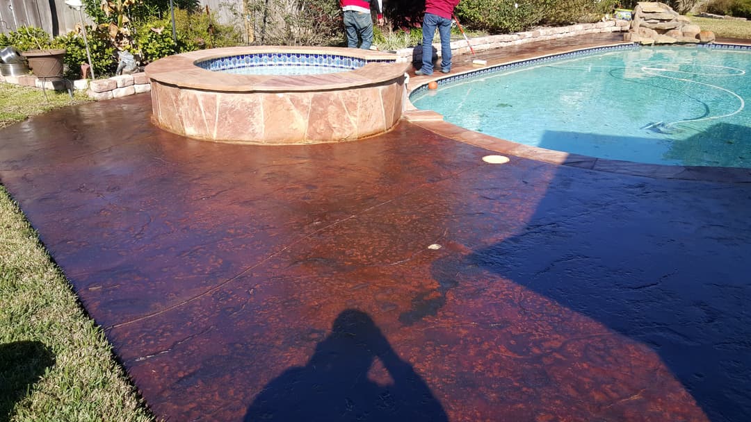 Poolside area with a spa, stamped concrete, and workers preparing the surface.