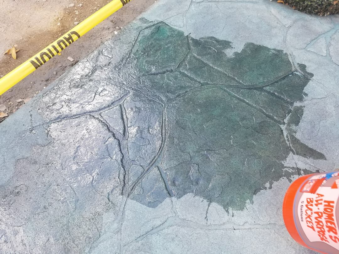 Concrete sidewalk with leaf pattern and construction caution tape, featuring an orange paint bucket.