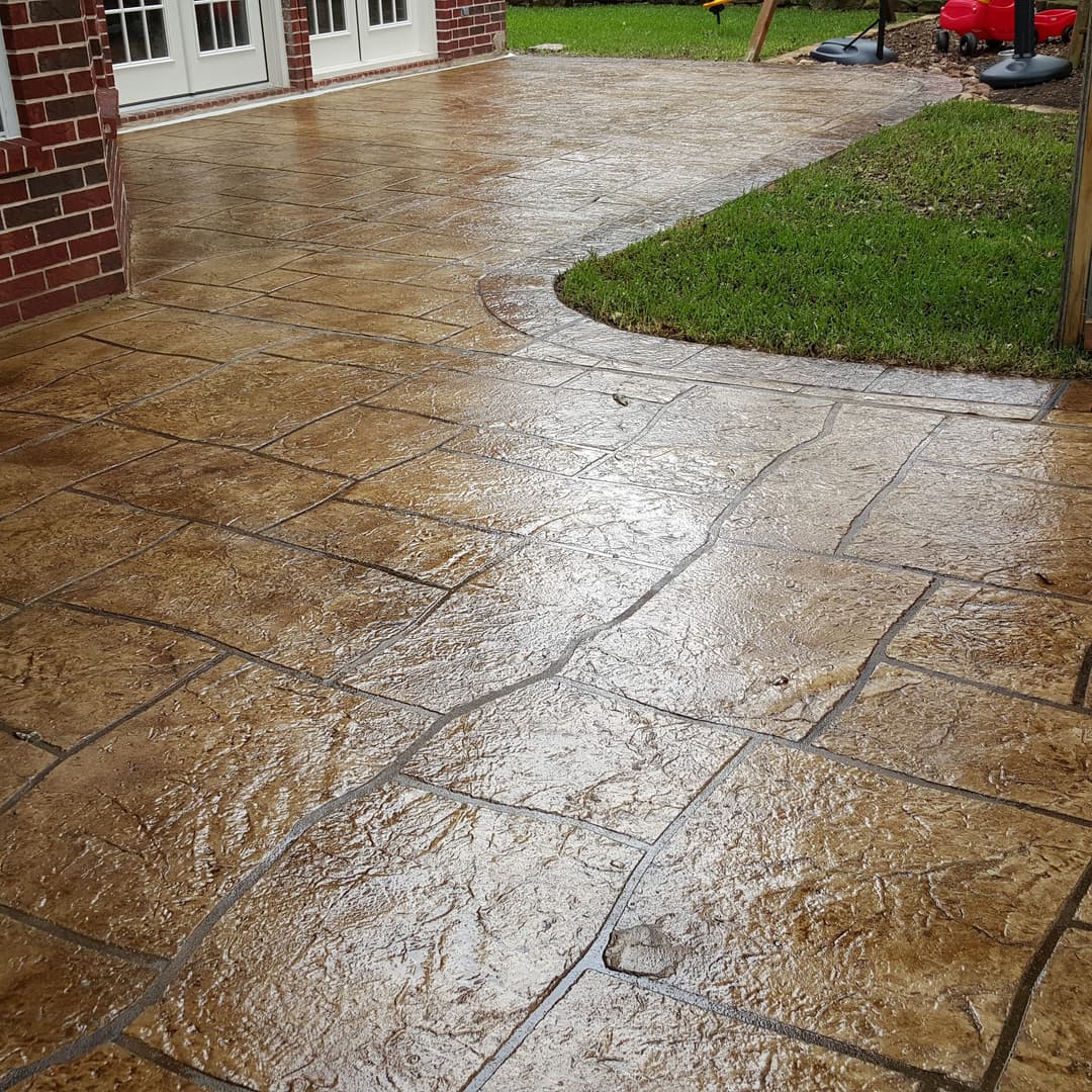 Textured stamped concrete patio with a sleek finish, showcasing a neat grass border.