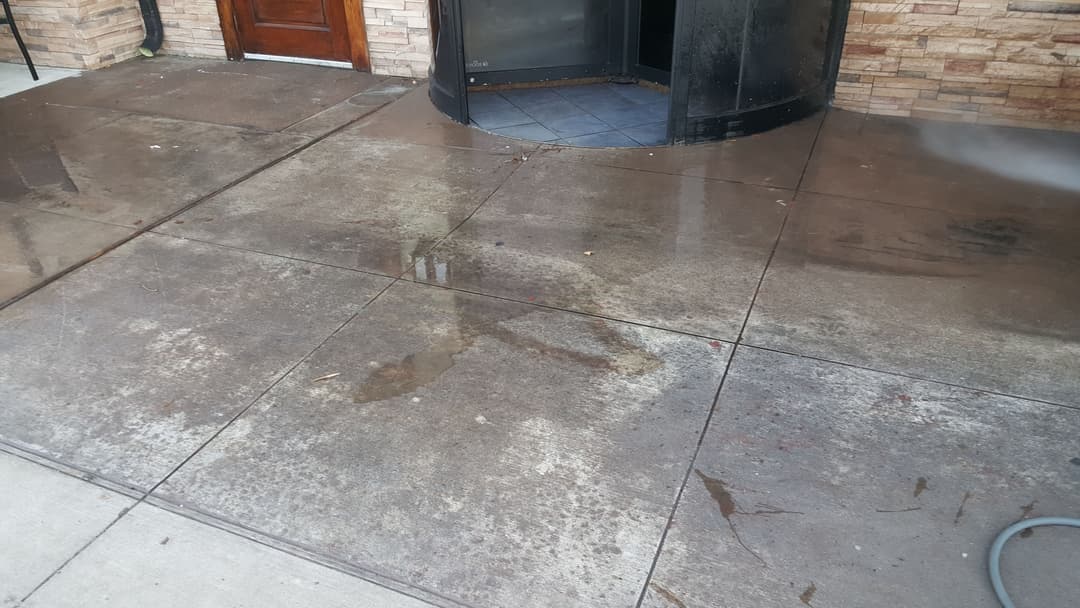 Wet concrete pavement outside a building entrance, showing uneven surface and puddles.