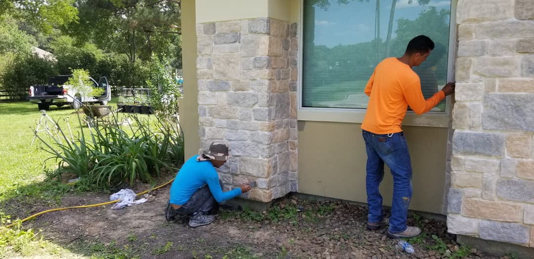 Workers applying stone finish to a home's exterior, showcasing craftsmanship and renovation efforts.