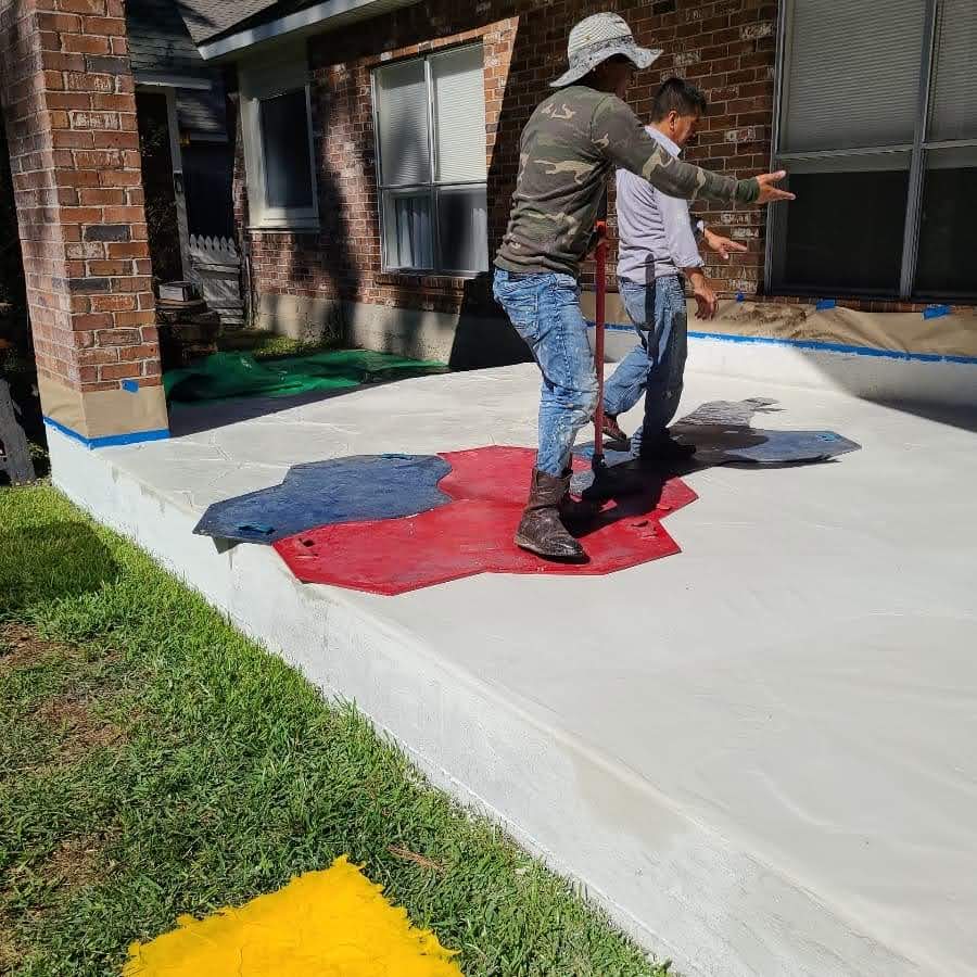 Workers applying colorful paint to a textured concrete surface in a residential outdoor setting.