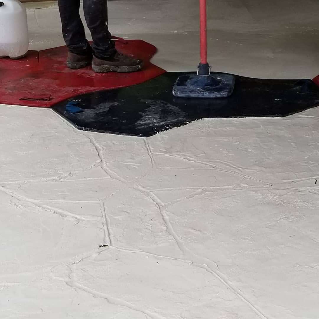 Worker applying a colored concrete finish on a patterned surface with a floor squeegee.