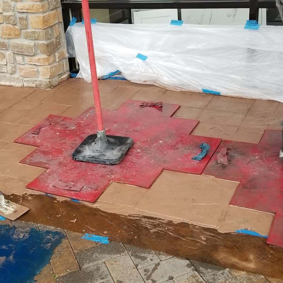 Installation of red concrete tiles with a trowel on a patio, featuring protective barriers.