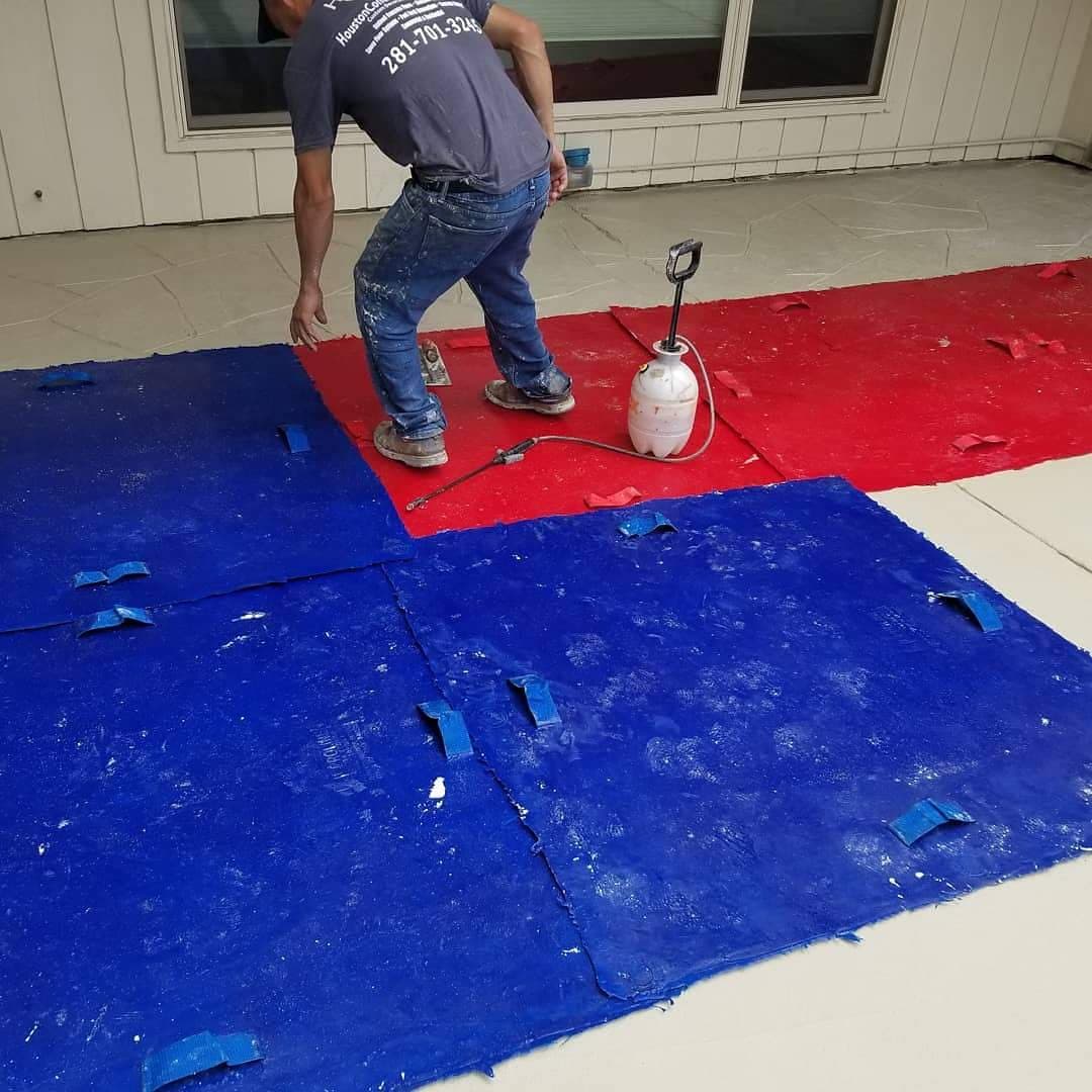 Worker applying red and blue paint on a textured surface outdoors using a spray tool.