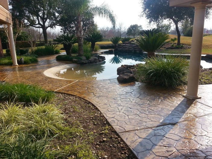 Lush garden landscape with stone pathway and pool surrounded by palm trees and greenery.