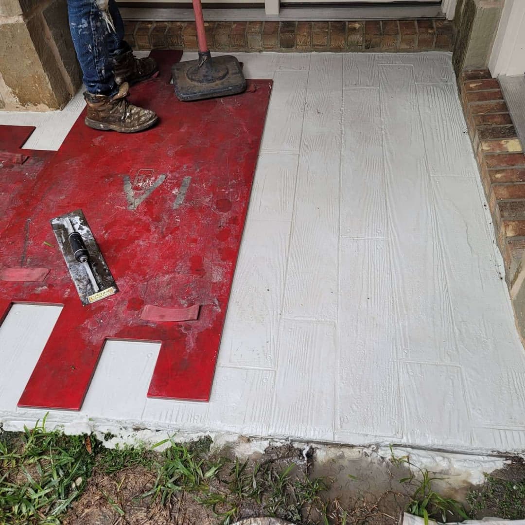 Person applying textured concrete overlay on outdoor surface with tools.