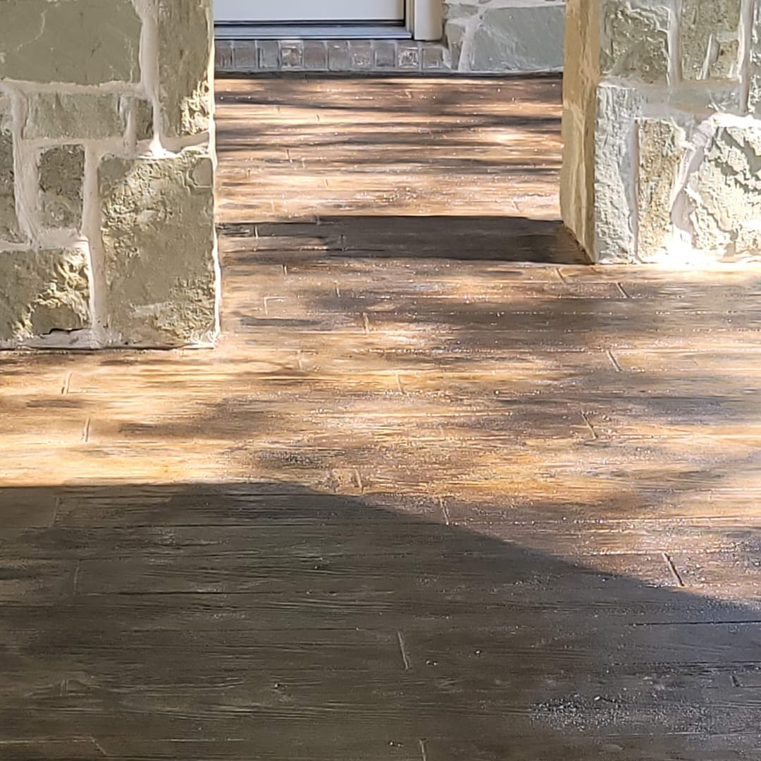 Sunlit stone patio leading to a doorway, showcasing textured wooden flooring.