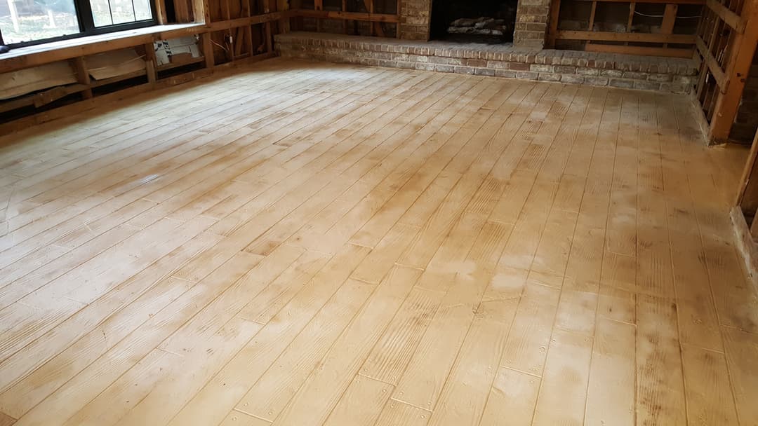 Unfinished wooden floor in a rustic interior space with exposed brick fireplace.