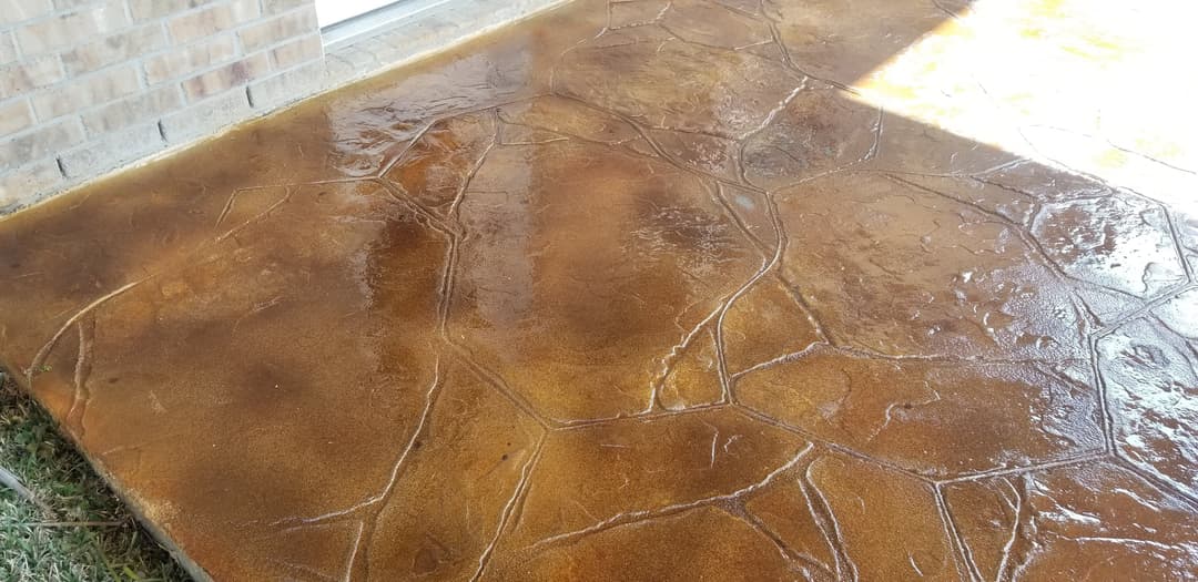 Decorative stamped concrete patio with a brown finish and wet surface, highlighting texture.