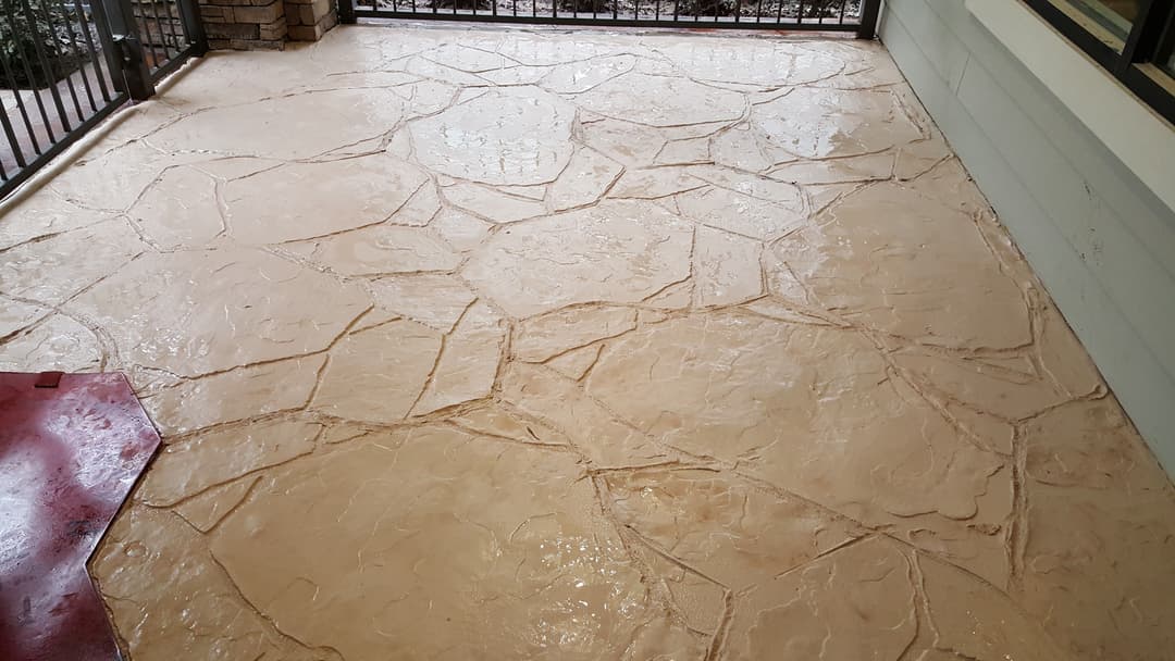 Decorative stamped concrete patio with a stone pattern, wet surface reflecting light.