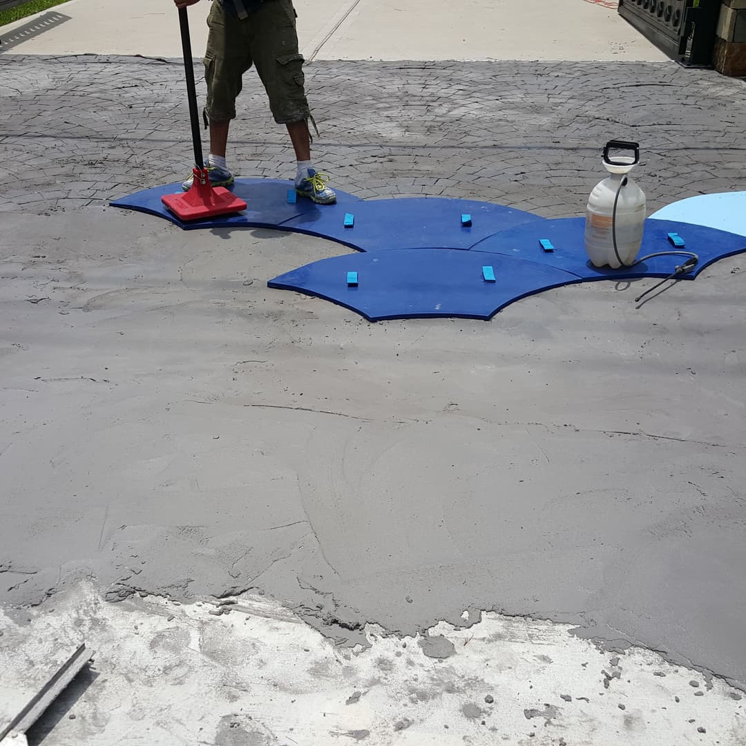 Person applying a decorative concrete overlay with blue shapes on a textured surface.