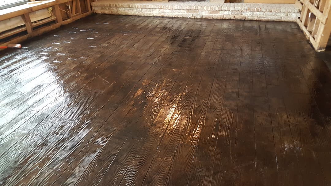Shiny, newly finished wooden floor in a room with exposed brick walls and sunlight.