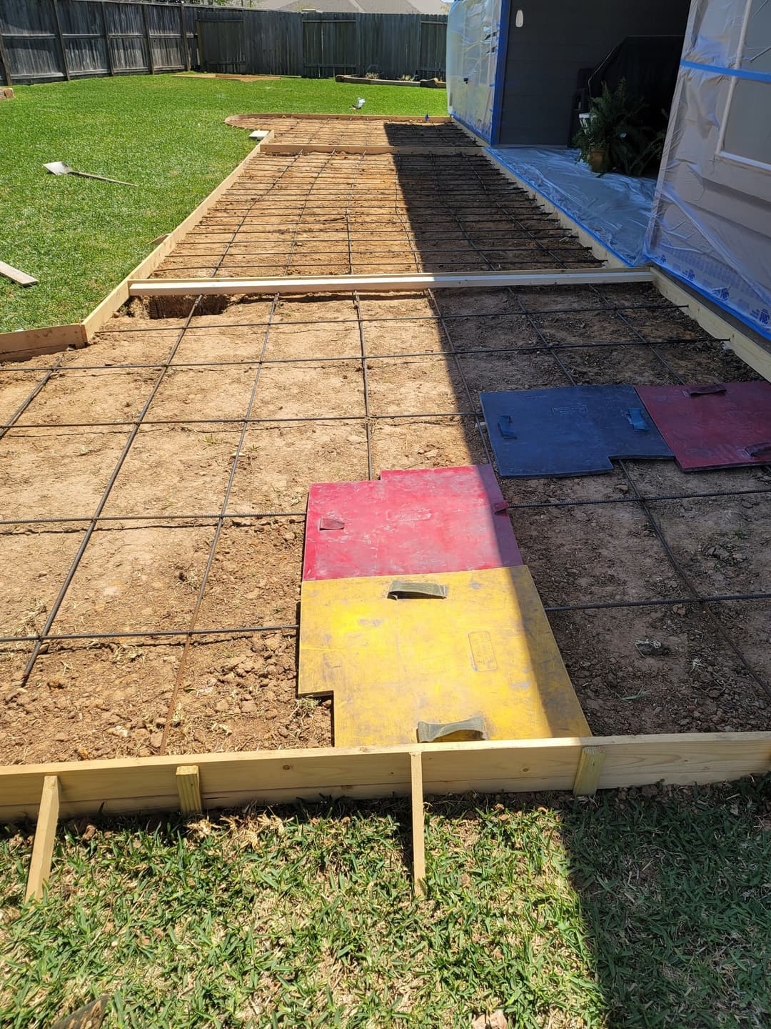 Concrete slab preparation with rebar grid and color-coded safety mats on grassy surface.