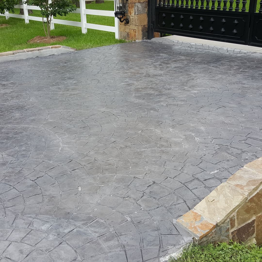 Stamped concrete driveway with a decorative pattern, stone border, and lush green lawn.