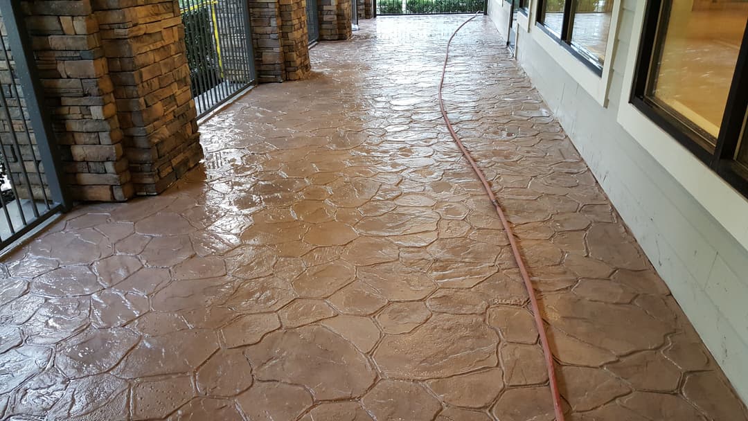 Textured concrete patio with a wet surface and a hose along the side of the house.