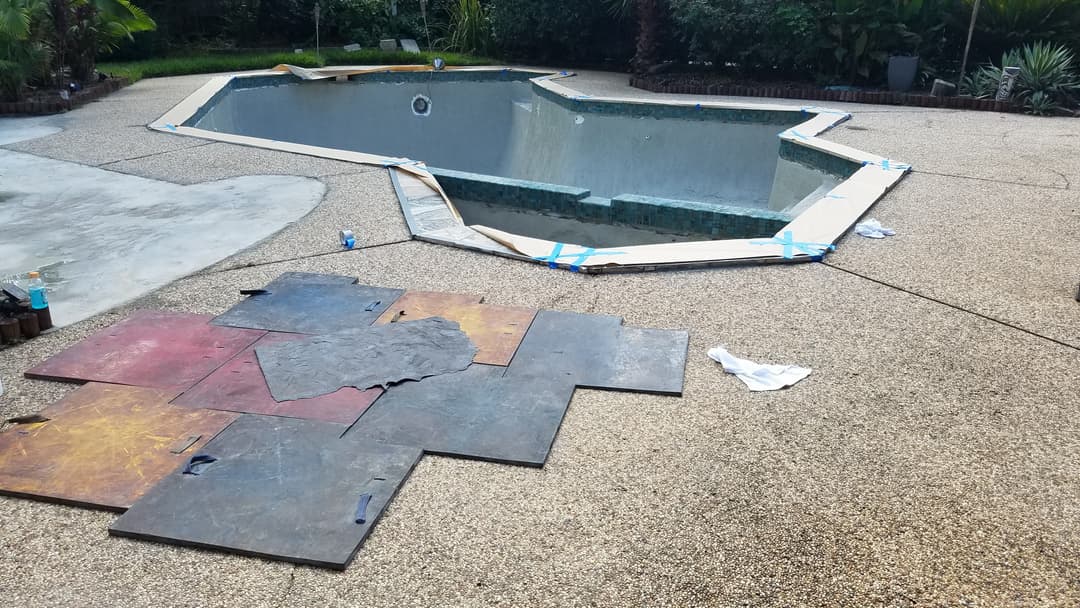 In-ground swimming pool under construction with surrounding textured concrete and materials.