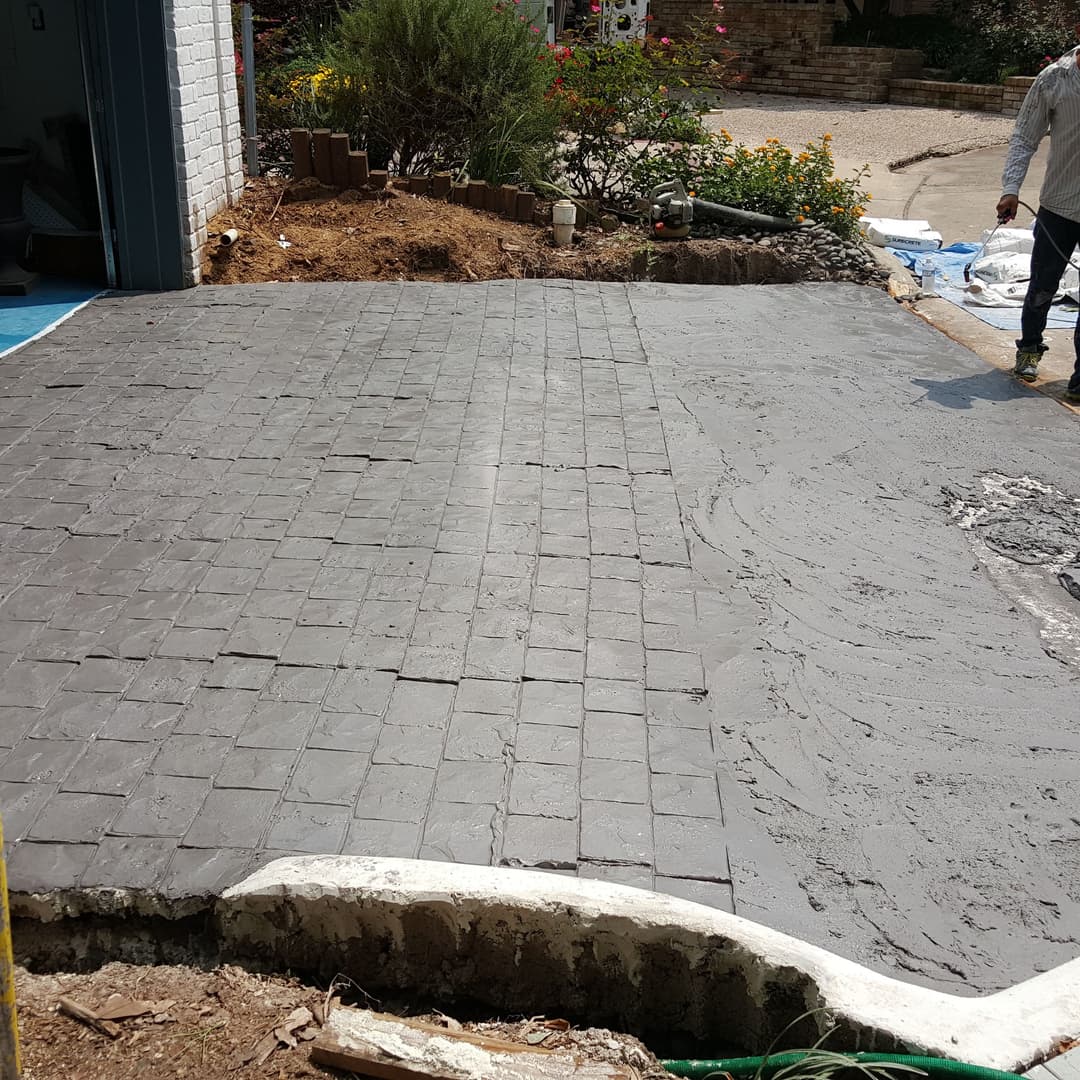 Freshly laid gray stamped concrete patio with a worker finishing the edges.