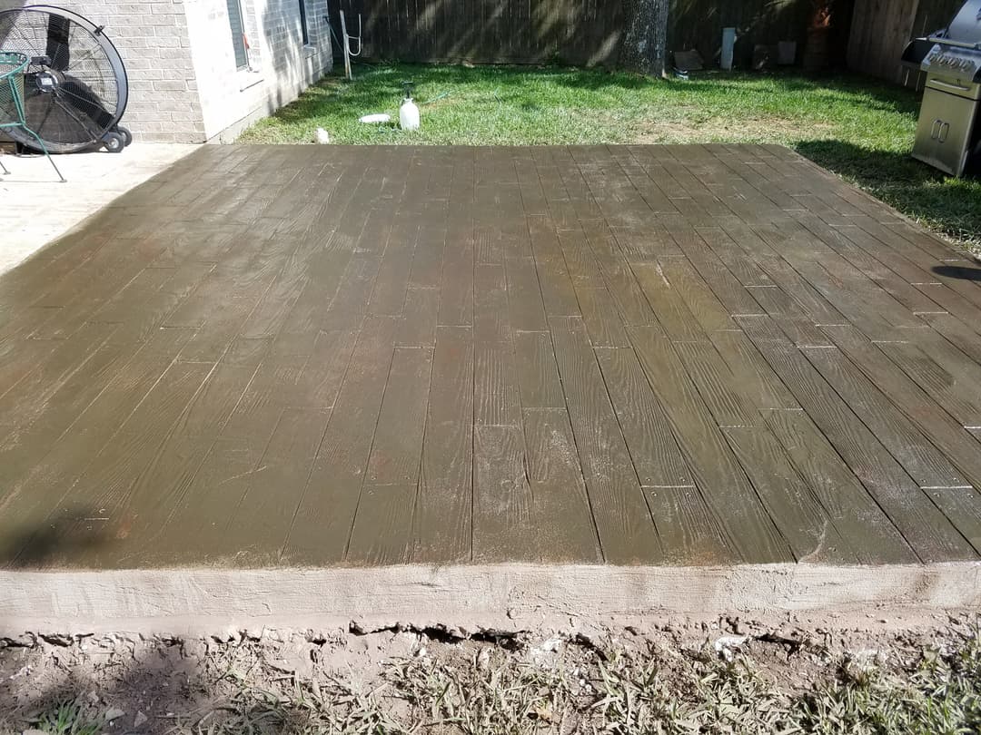 Concrete patio with a wood plank texture, freshly poured and leveled in a backyard setting.