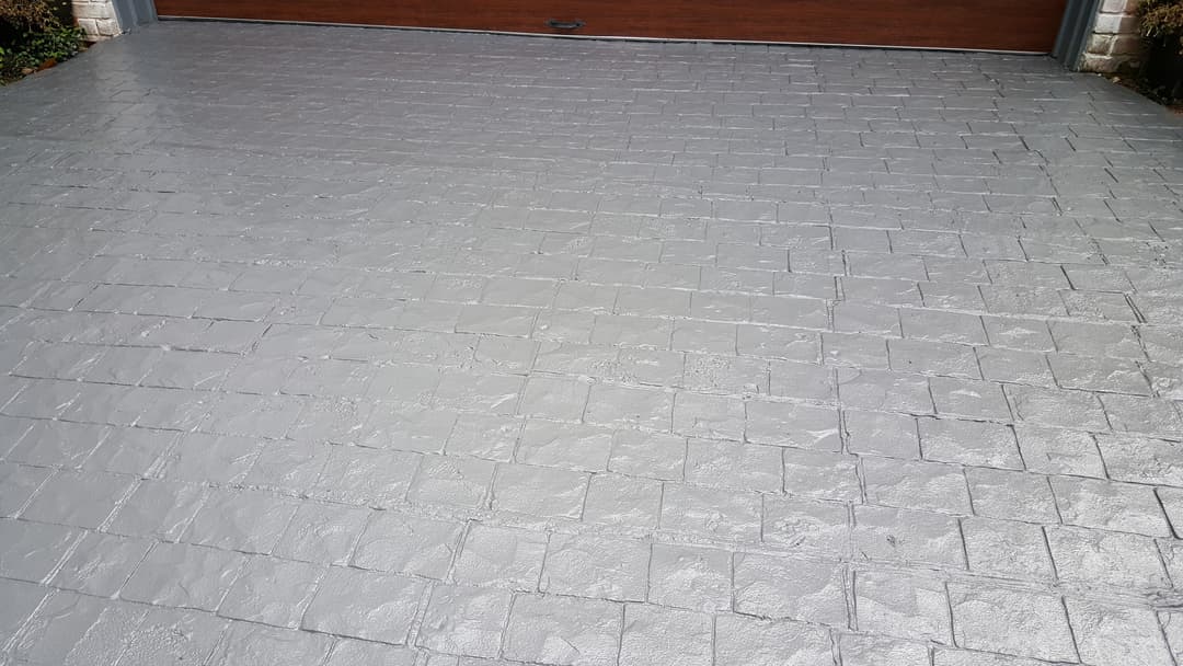 Textured gray stamped concrete driveway with a garage door in the background.