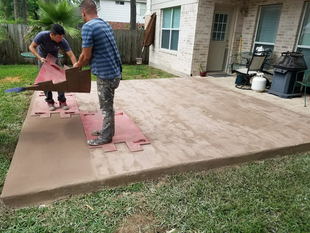 Workers installing a concrete patio slab in a residential backyard.
