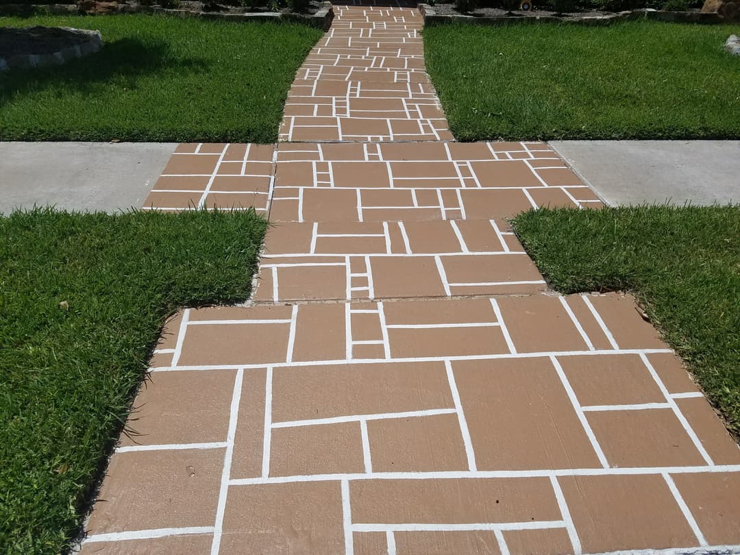 Decorative concrete pathway with white lines, surrounded by green grass in a landscaped yard.