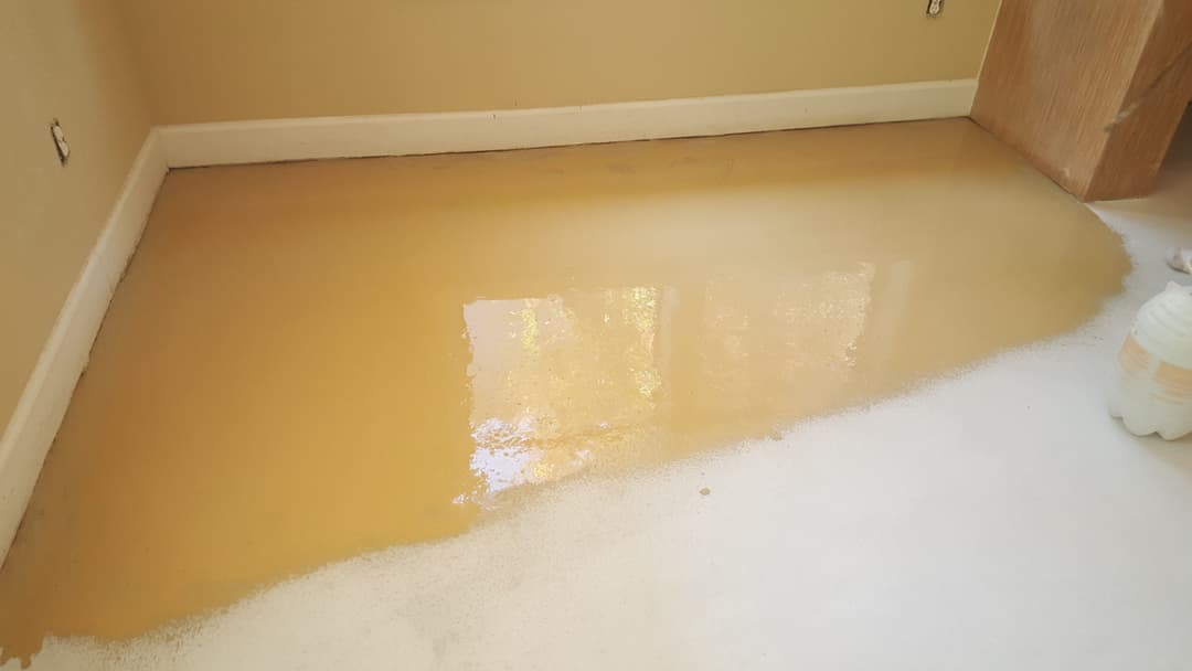 Room undergoing floor coating application with a glossy, yellowed finish.