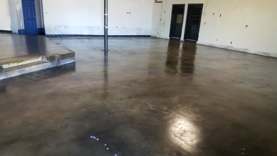 Polished concrete floor in an empty industrial space with black doors and clear walls.