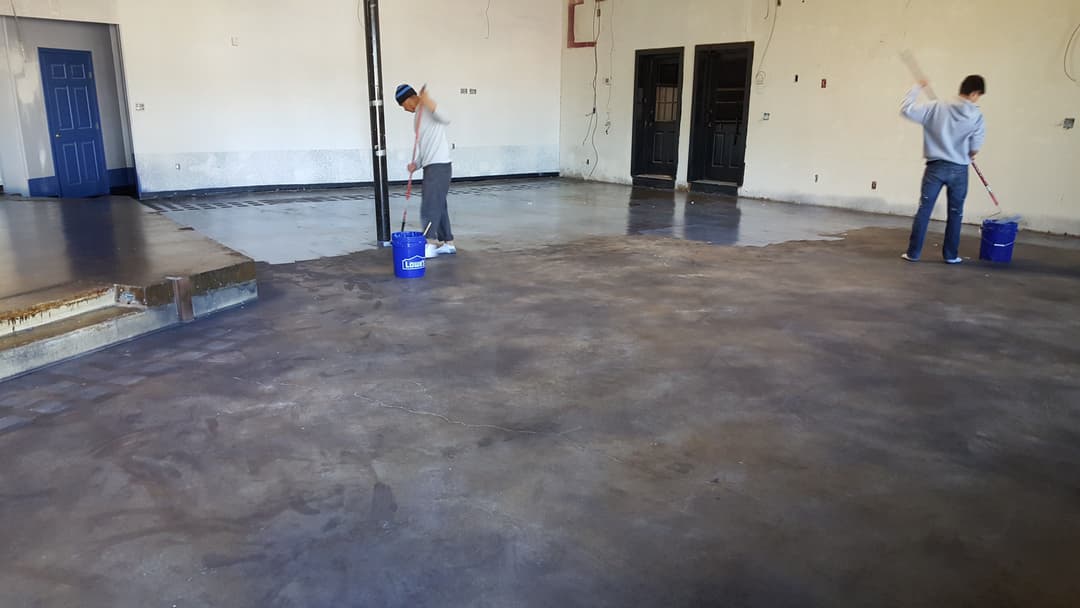 Workers applying floor coating in a spacious warehouse with concrete surface.