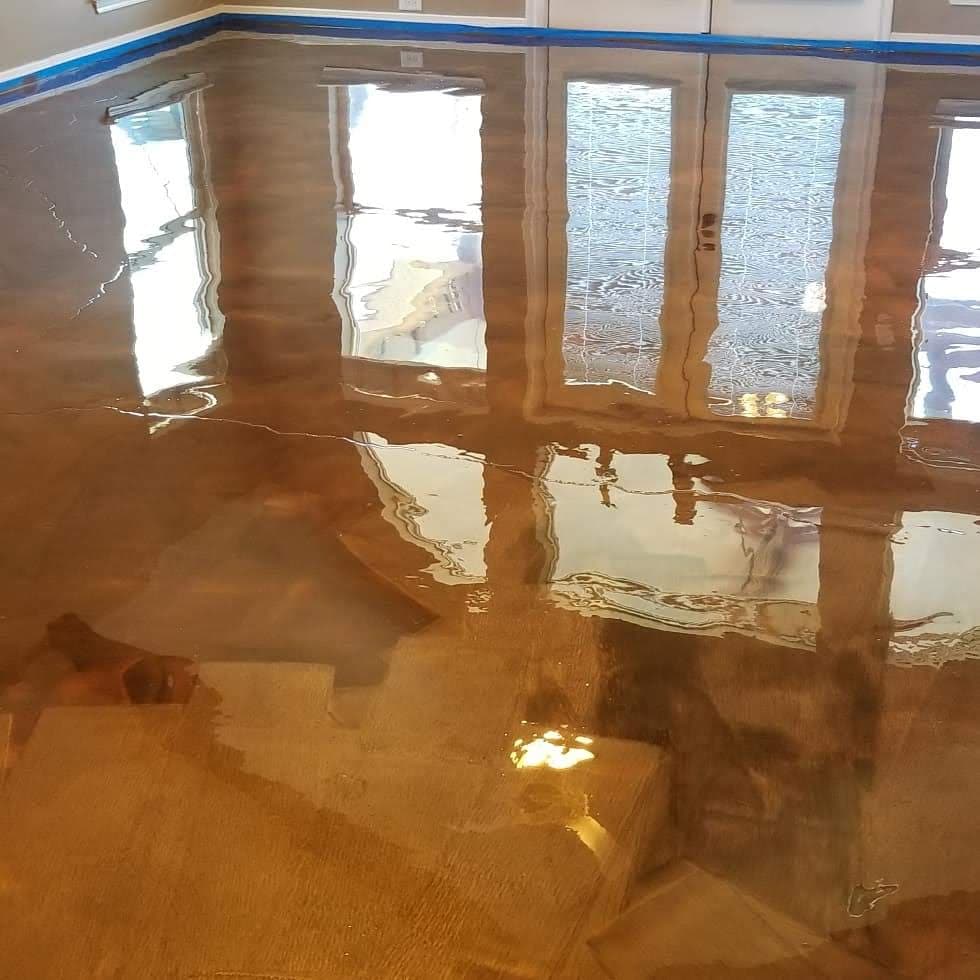 Glossy epoxy floor coating in a well-lit room with large windows. Reflective surface details.