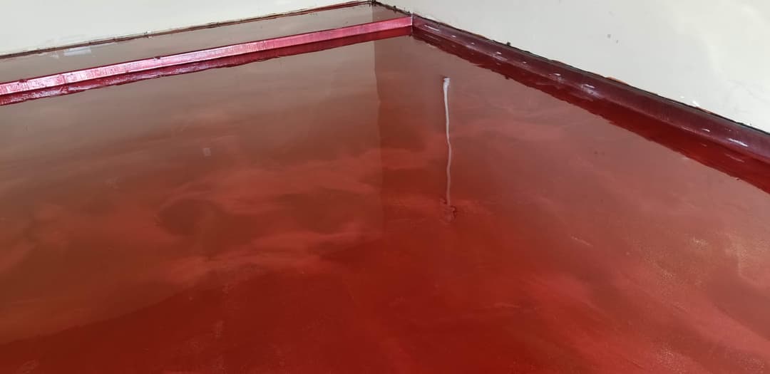 Polished red epoxy floor in a corner of a room, showcasing a glossy finish and smooth surface.