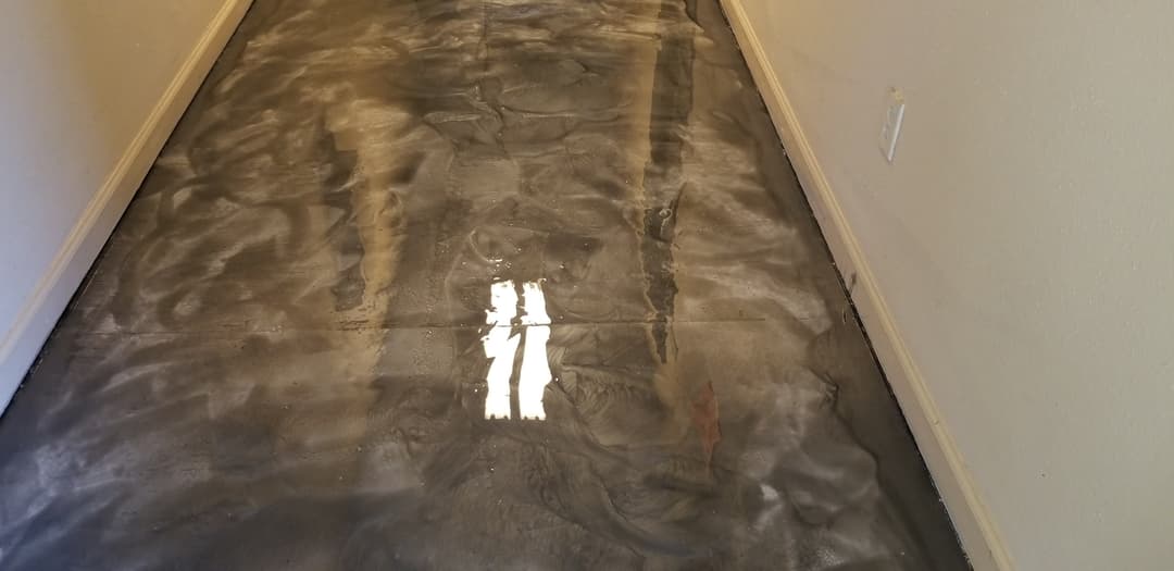 Shiny, freshly poured concrete floor in a residential hallway with warm lighting.