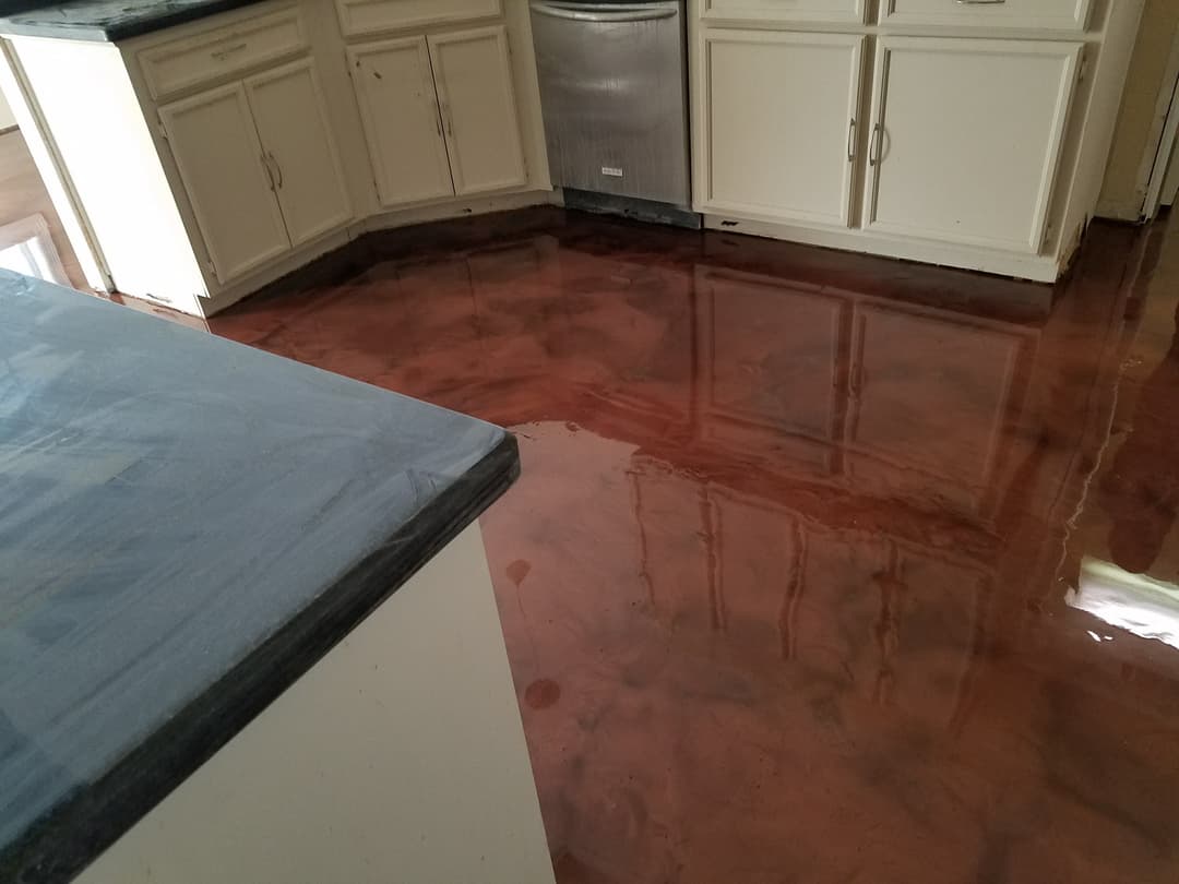 Flooded kitchen with shiny reddish floor and white cabinets, highlighting water damage.