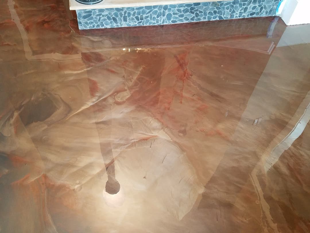 Polished epoxy floor with rich brown tones and stone wall in background. Contemporary interior.