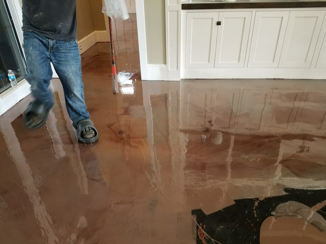 Worker applying epoxy resin coating on floor with glossy finish in residential space.