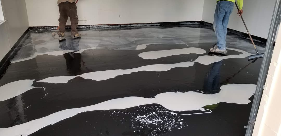 Workers applying black and white epoxy flooring in an indoor space.