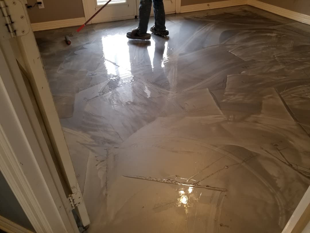 Worker applying a glossy finish to a newly polished concrete floor in a residential space.