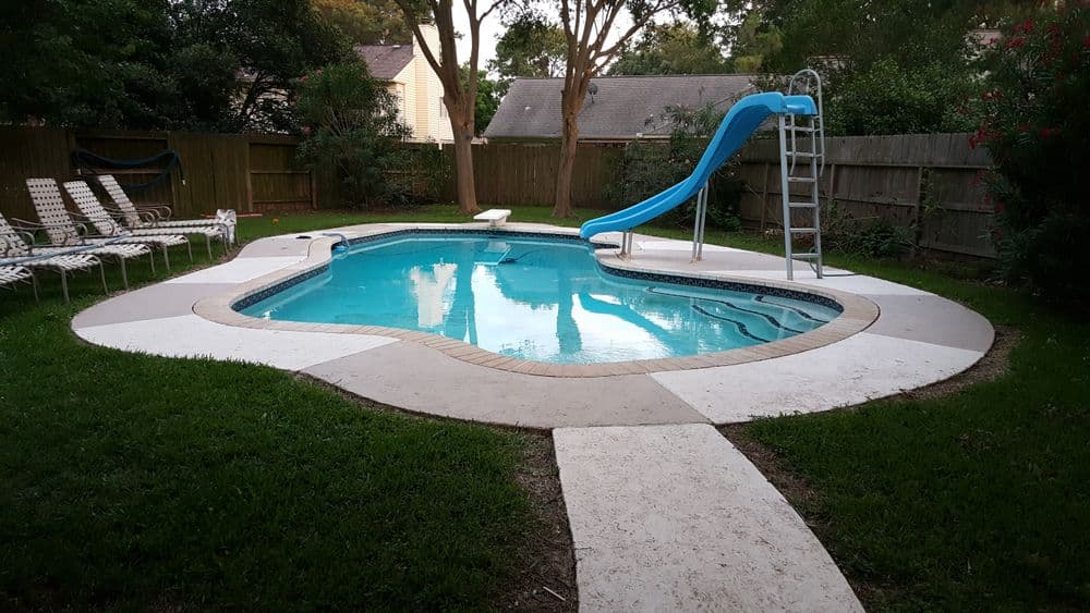 Backyard pool with a blue slide, surrounded by lounge chairs and lush greenery.