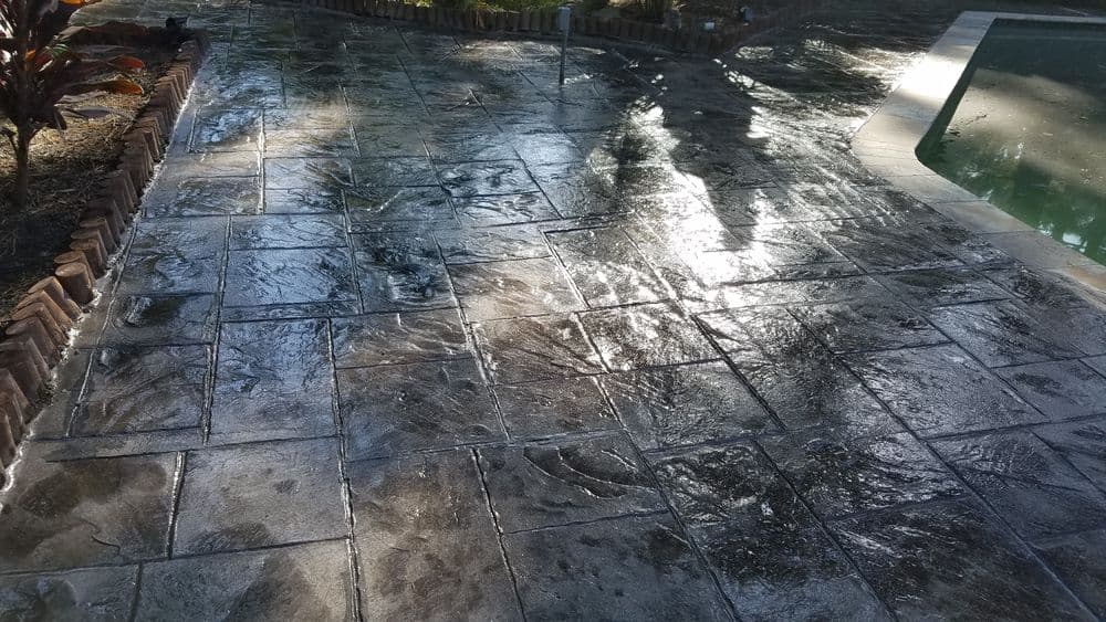 Stamped and finished concrete patio glistening in sunlight near a swimming pool.