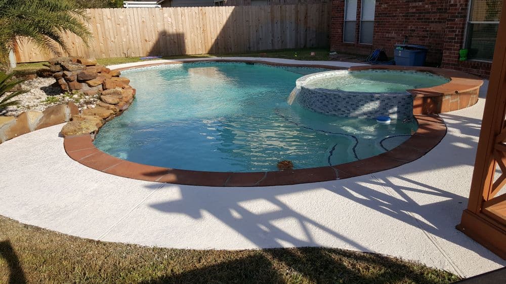 Backyard pool with spa, stone accents, and patio area in a sunlit setting.